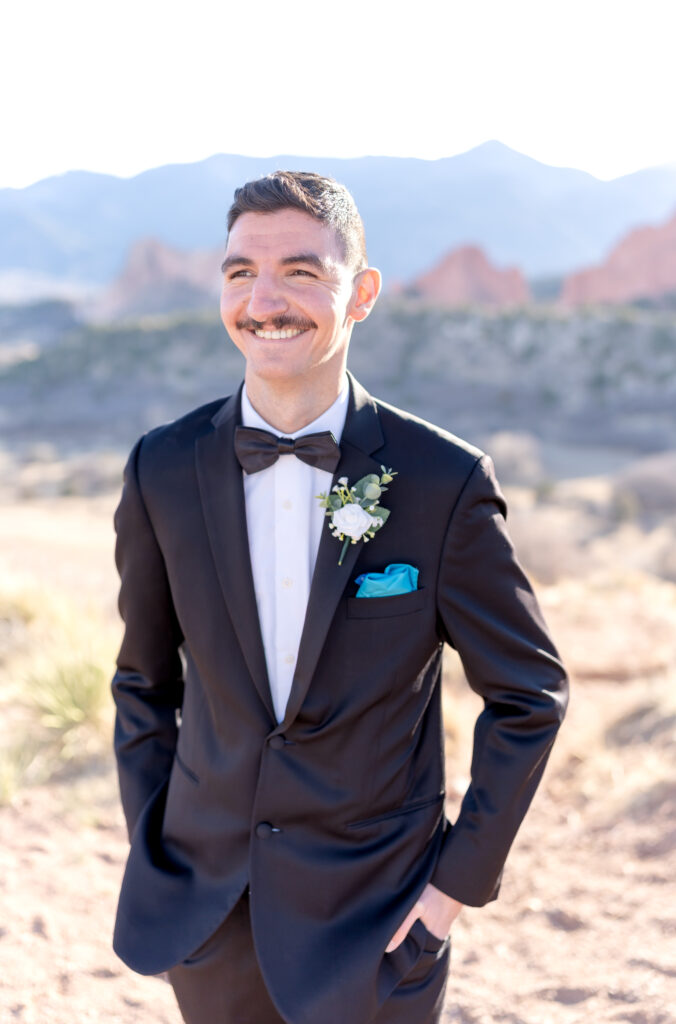 Groom standing and smiling out in the distance while putting his hands in his pant pockets