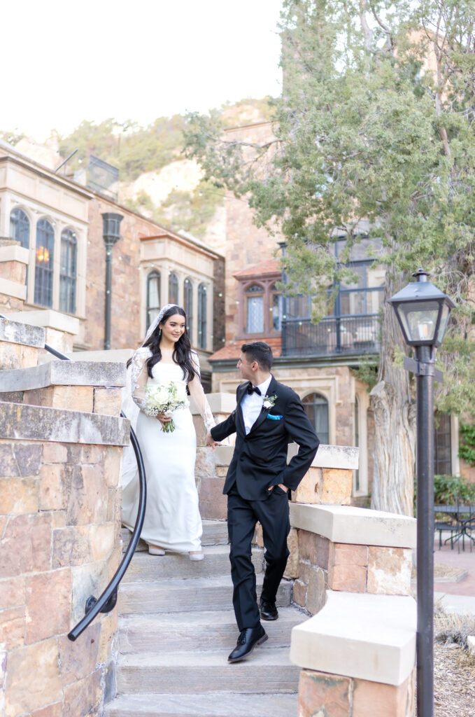 Groom holds his bride's hands as he leads her down the winding steps of Glen Eyrie Castle on their elopement day
