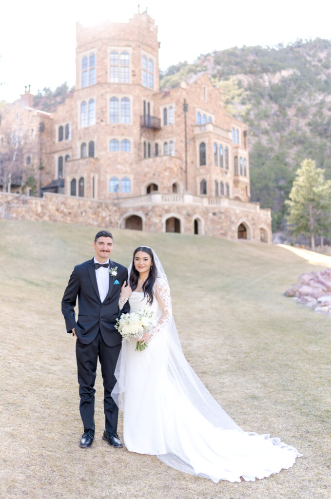Bride and groom standing on the lawn with Glen Eyrie Castle in the background