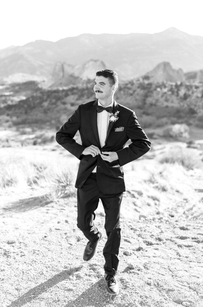 Portrait of groom walking while buttoning up his black jacket on his Colorado Springs elopement day
