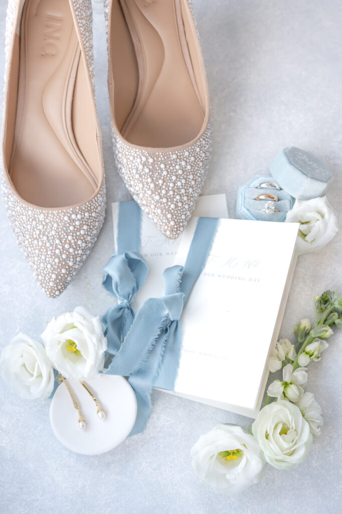 Wedding detail photo of bride's shoes, vow books, jewelry, and white florals