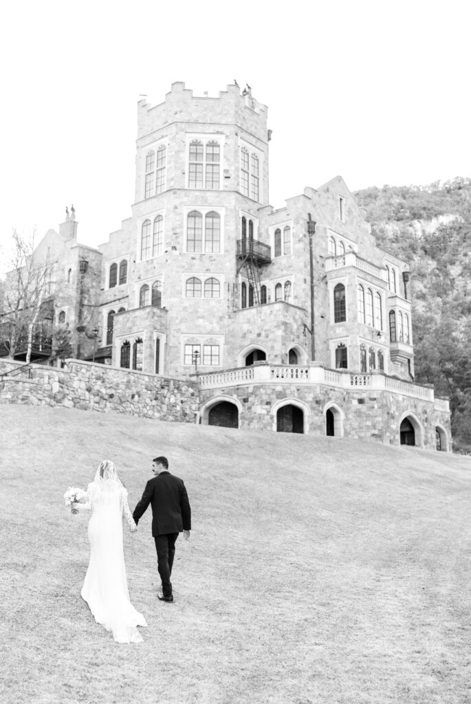 Bride and groom hold hands as they walk up toward the castle at Glen Eyrie Castle in Colorado Springs, Colorado