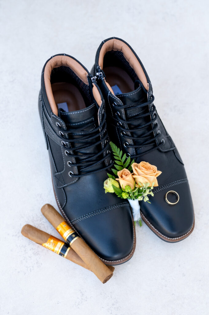 Wedding detail photo of the groom's boutonniere and wedding ring laying on top his shoes with cigar next to the shoes