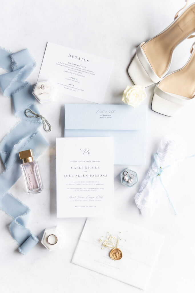 Wedding detail photos of wedding announcements with rings, perfume,  and flowers arranged throughout