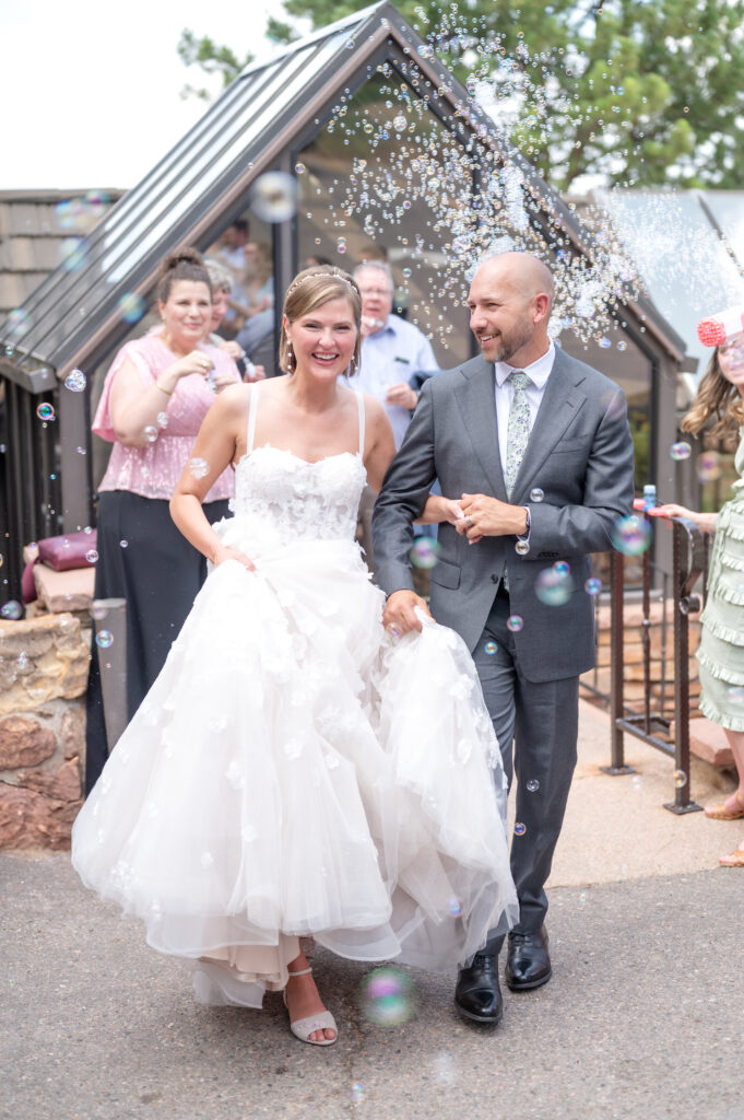 Bride and groom laughing as they make their exit Flagstaff House Boulder together while the wedding guests blow bubbles around them
