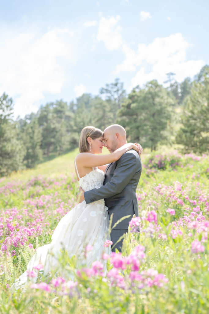 Newly married couple stand together in a wildflower meadow touching foreheads