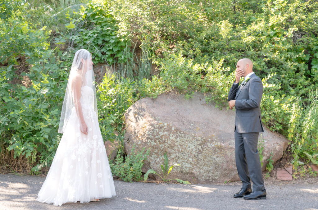 Groom covers his mouth with his hand as his bride approaches in her gown and veil during their first look