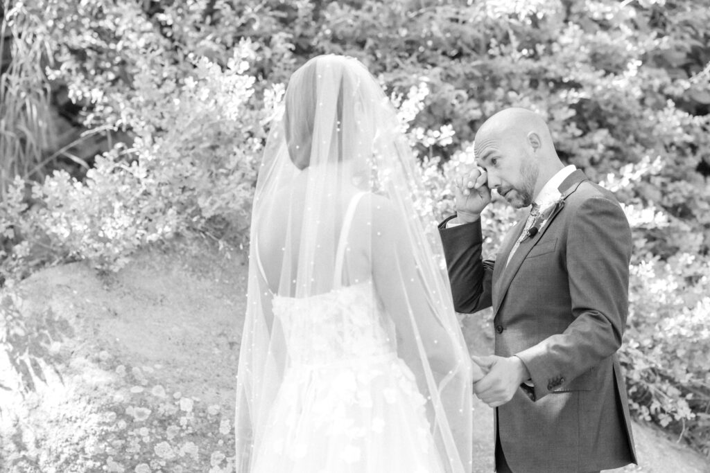 Groom wipes his eyes as he takes his bride's hand during their wedding first look in Colorado