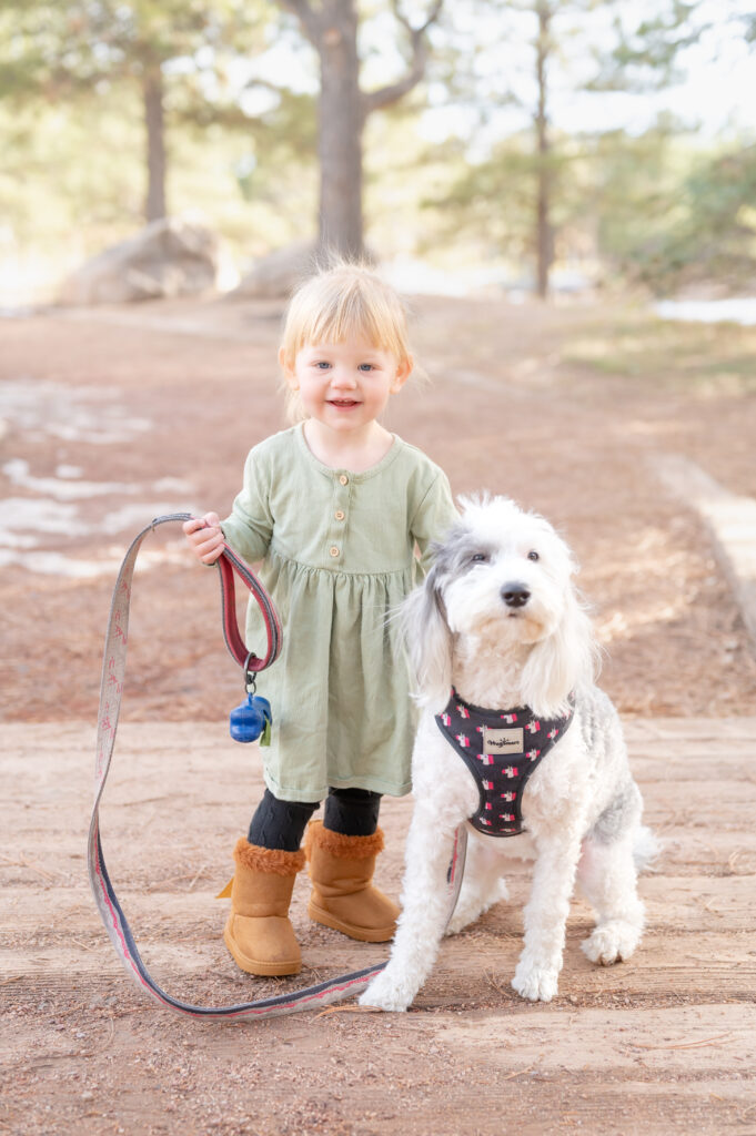Little girl smiling and holding her dog's leash with one hand while she pats his head with the other