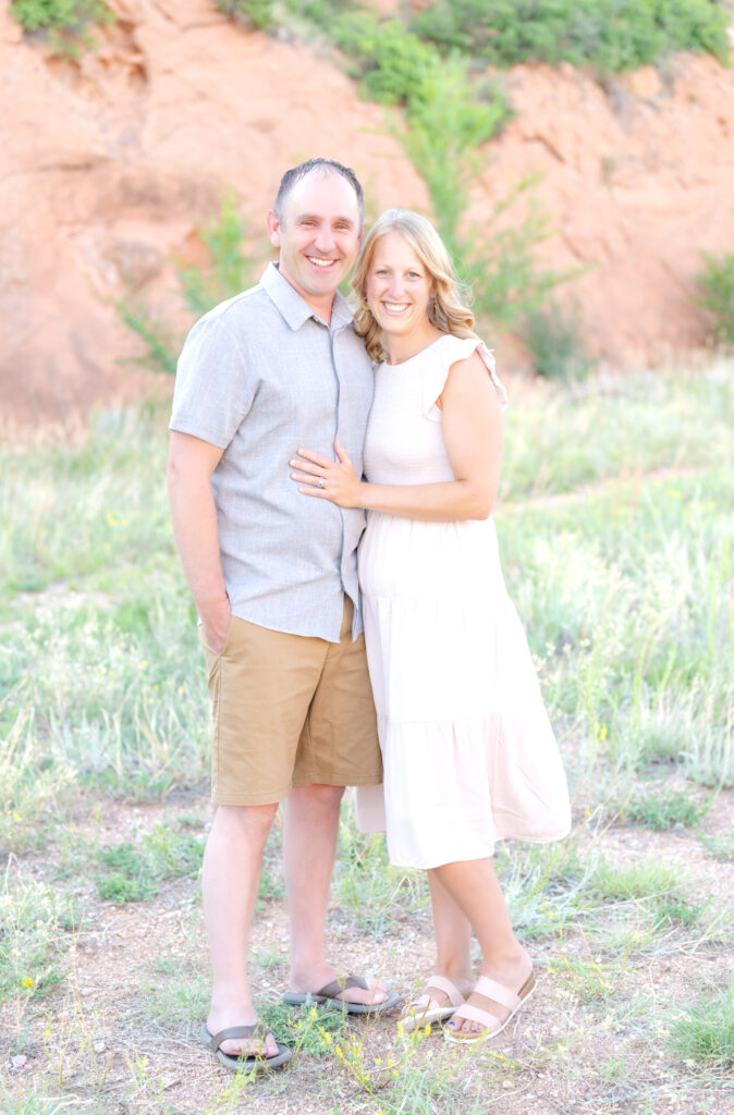 Mom and Dad pose in a field of wildflowers against a red cliff in Colorado Springs during their family photoshoot
