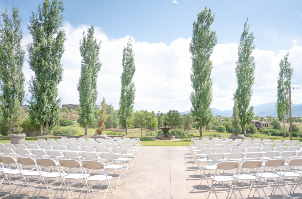 Rows of chairs set up on a pavilion at the Flying Horse Resort in Colorado Springs with a fountain, lush lawns, and trees as the backdrop for a wedding ceremony