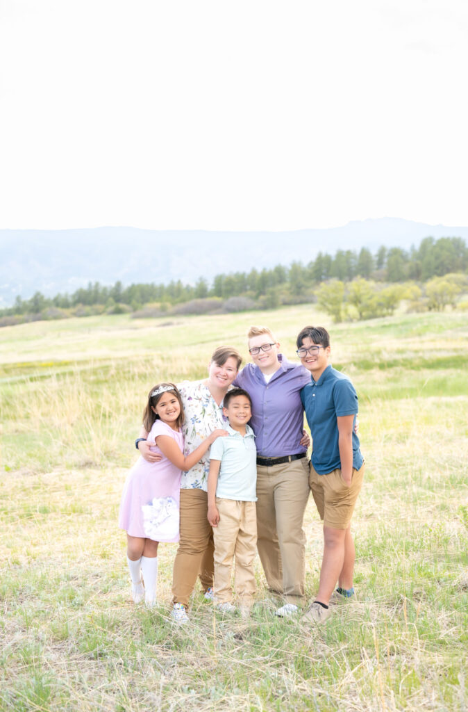 Two moms smiling with their daughter and two sons in grassy meadow field during their family photoshoot in Colorado Springs 