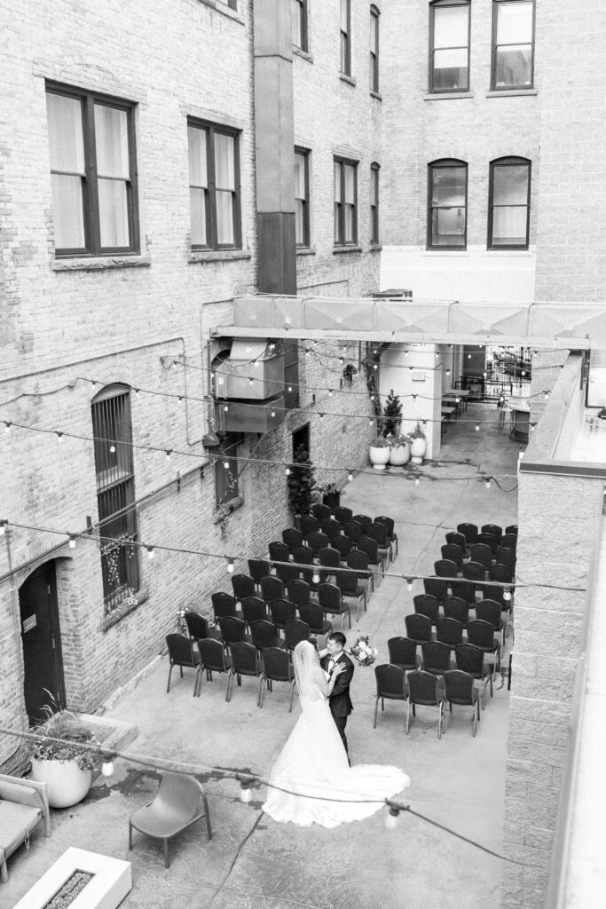 Birds-eye view of bride and groom dancing together under strings of light in an empty wedding venue