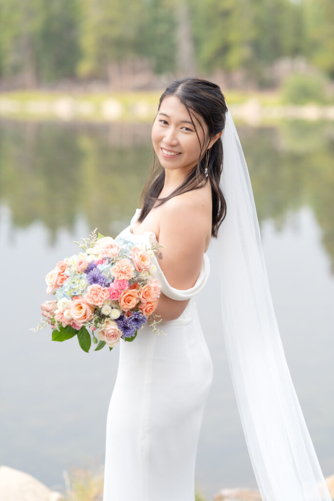 Bride with long flowing veil and bouquet of roses standing by Echo Lake in Evergreen Colorado