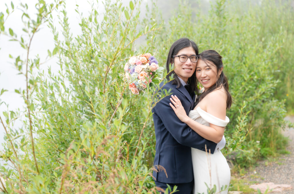 Bride and groom pose together among the greenery at the edge of Echo Lake Colorado on their elopement day