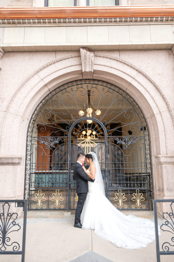 Newly married couple standing together outside a wrought-iron archway entrance to the Mining Exchange Hotel in Colorado Springs
