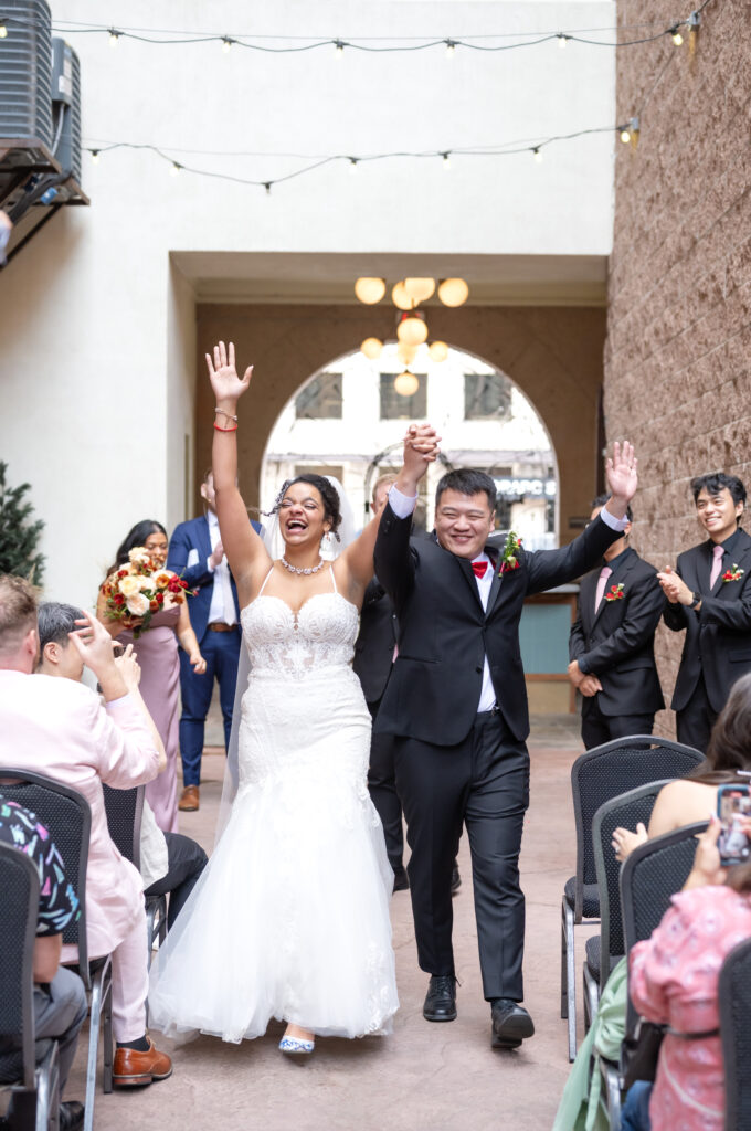 Bride and groom holding hands and laughing as they walk down the aisle together after their wedding ceremony to applause from friends and family