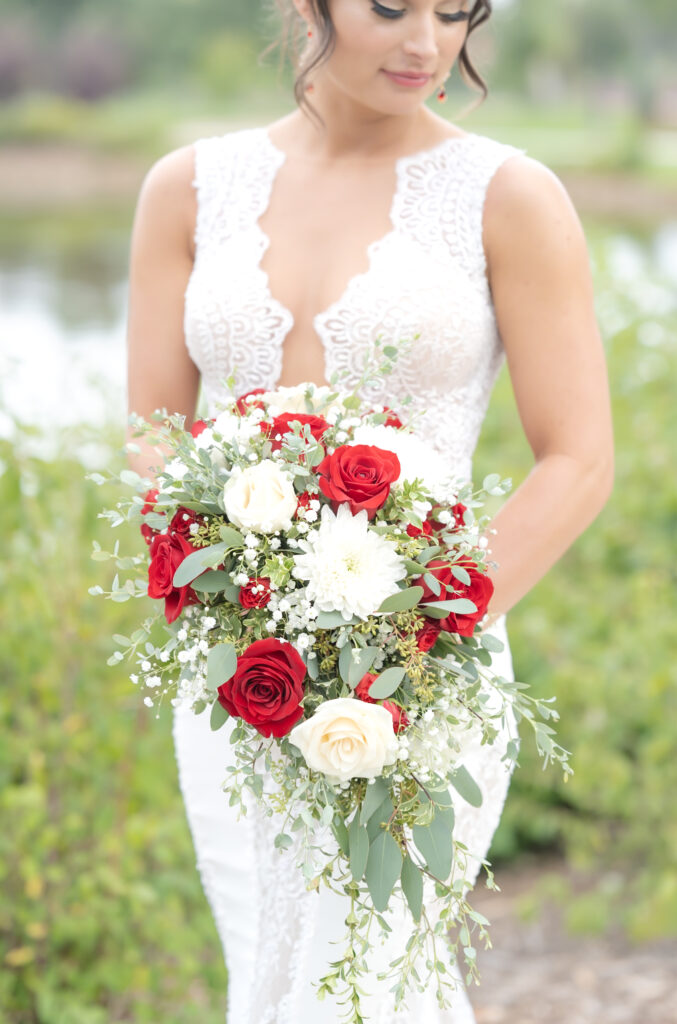 Bride holding her bridal bouquet on colorado pinery wedding day with greenery, white and red florals