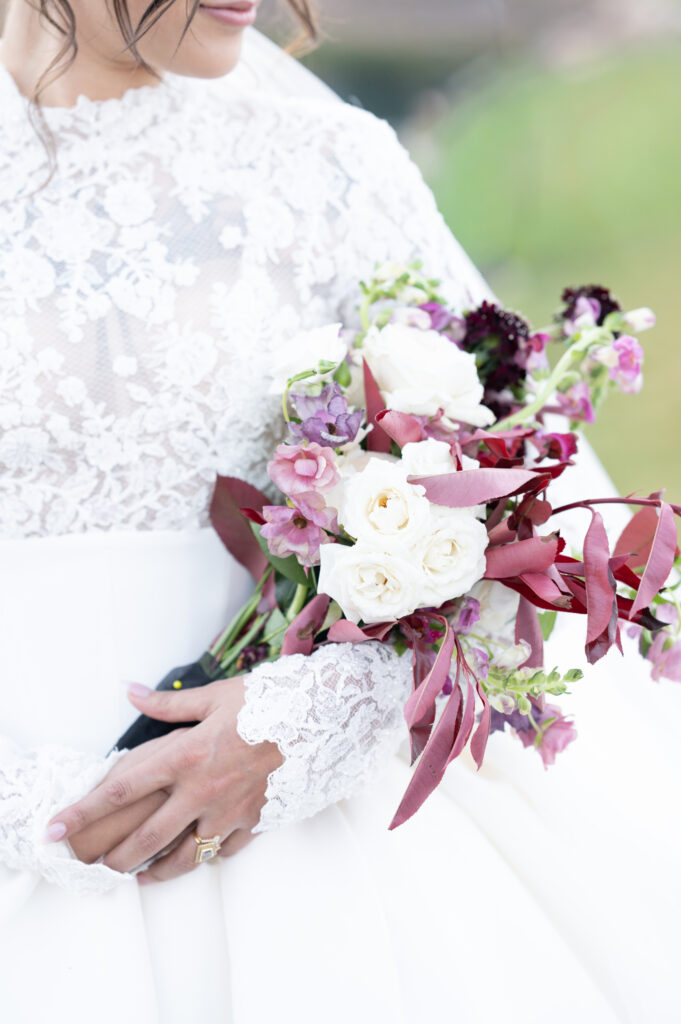 Detail portrait of the Bride holding her maroon, green, and white bridal bouquet into her elbow