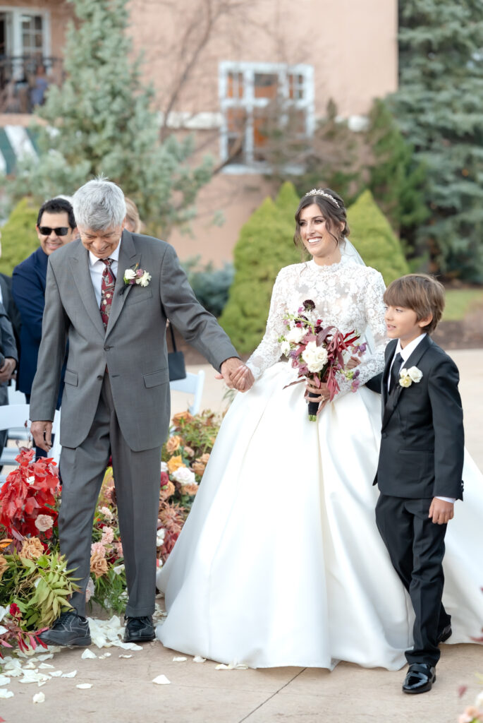 Bride walking down the aisle holding her father's hand and her son on their colorado springs winter wedding day 