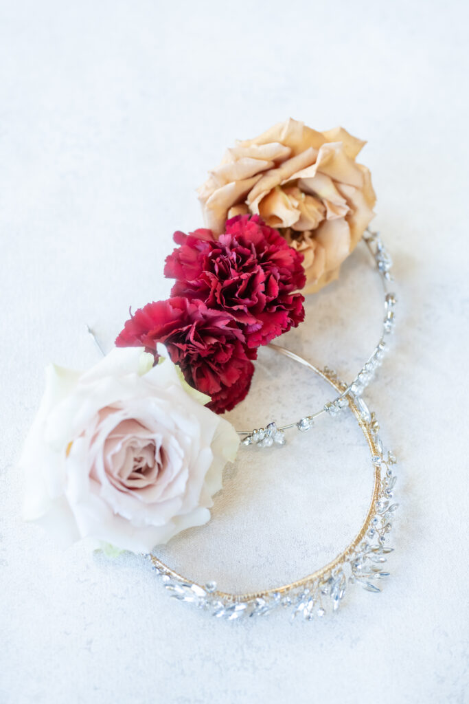 Flat lay of bridal wedding details featuring white, red, and orange florals laying on top of bride's bridal headband at The Broadmoor