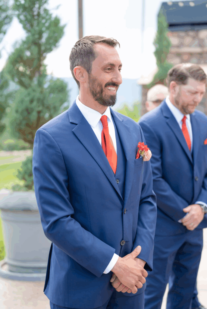 groom watching his bride walk down the aisle, he is wearing a navy blue suit, photographed at his colorado springs outdoor wedding