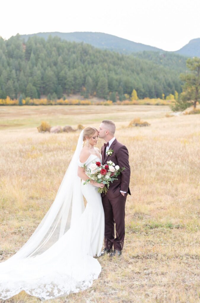 groom kissing bride and the forehead during their portrait session at their colorado springs outdoor wedding venue