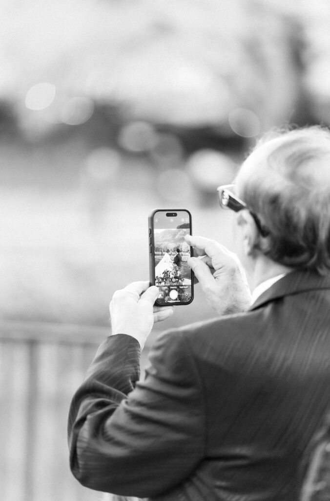 Editorial portrait of guest taking a photo on his phone to capture moment during wedding ceremony, at The Broadmoor