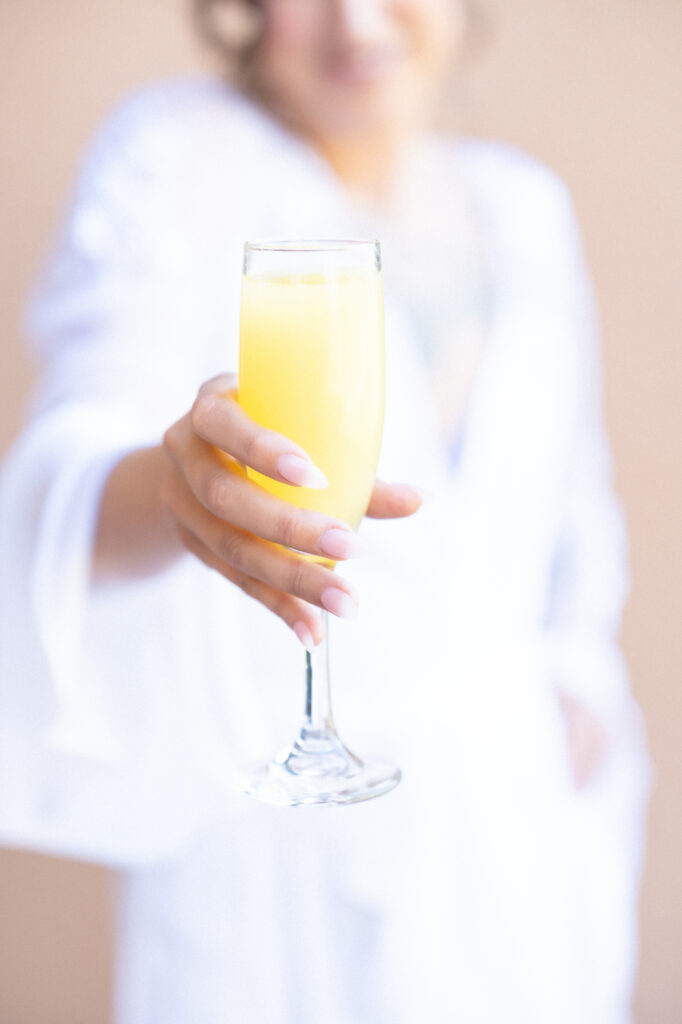 Bride holding her glass of mimosa while getting ready on her wedding day 