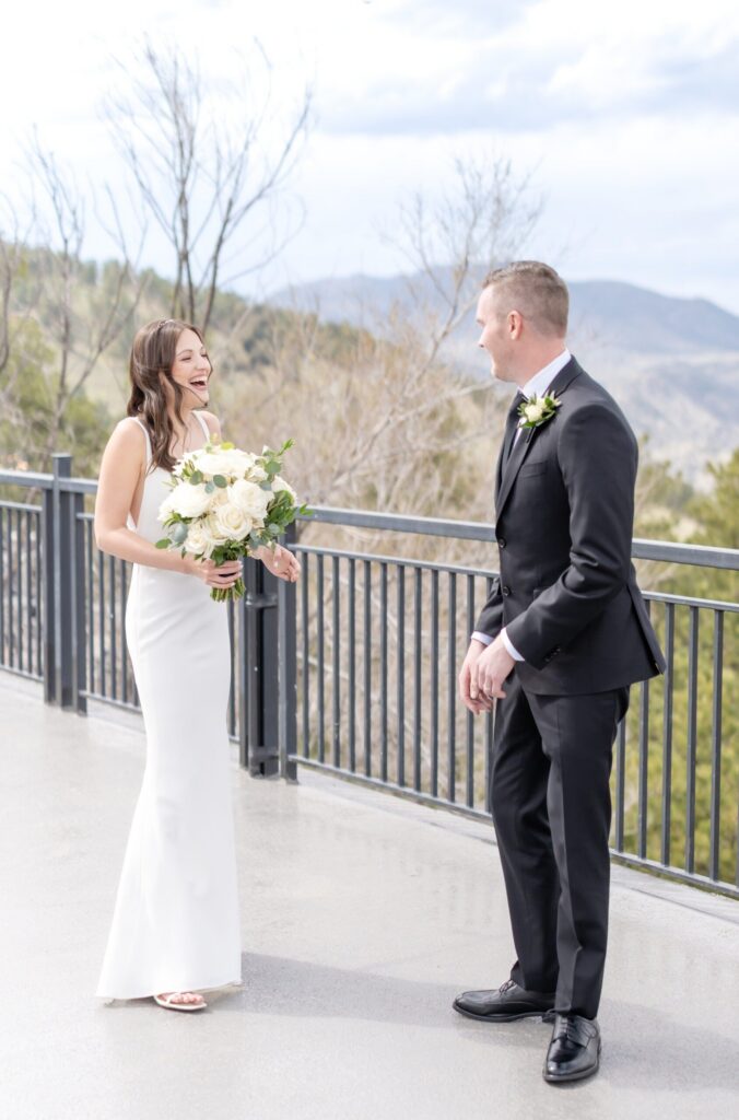 Bride and groom smiling and laughing together during their emotional first look on a mountain terrace in Colorado Springs overlooking the foothills.