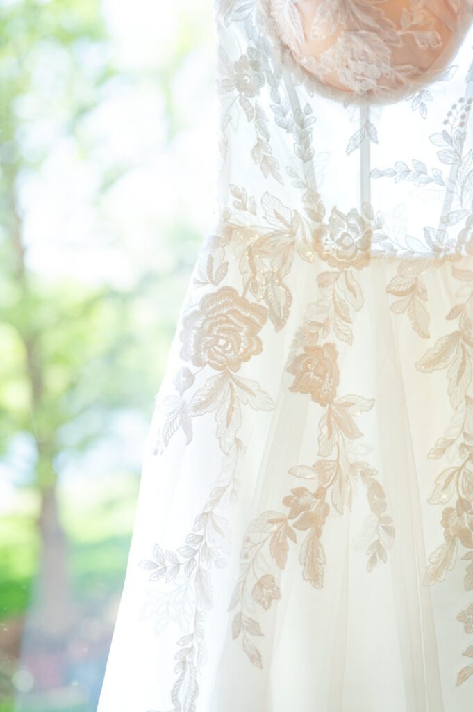 Close-up detail of a lace wedding gown with intricate floral embroidery and delicate sheer neckline illuminated by soft natural window light.