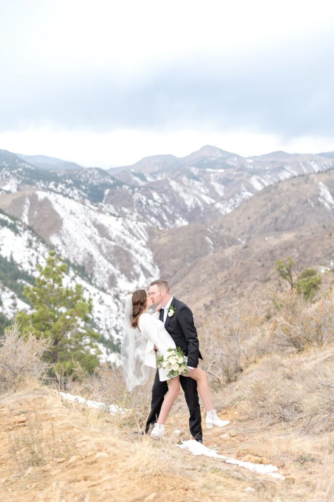 Newlywed couple sharing a kiss on a snowy Colorado Springs mountain overlook surrounded by dramatic peaks and soft winter light.