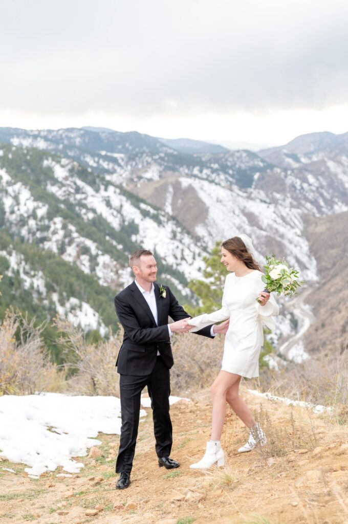 Bride holding a bouquet of ivory roses while walking hand in hand with her groom along a snowy mountain trail in the Colorado Springs foothills.