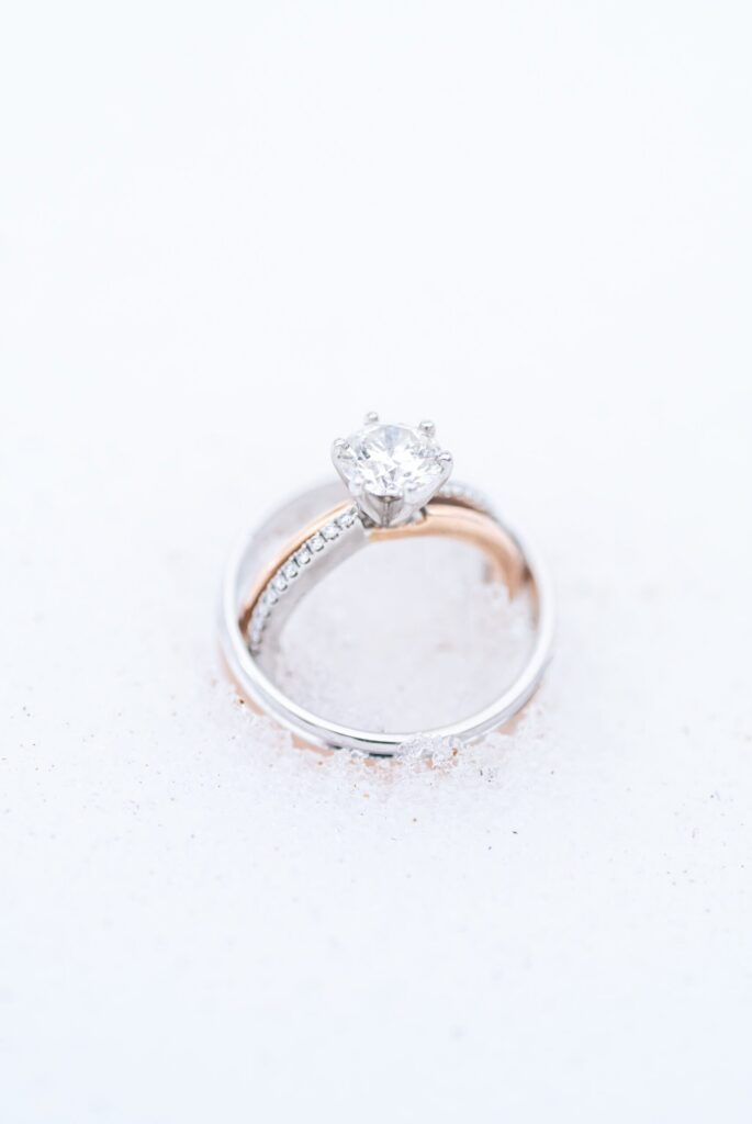 Round-cut diamond engagement ring with a pavé band nestled in fresh Colorado snow, captured in soft winter light for a romantic mountain wedding detail.