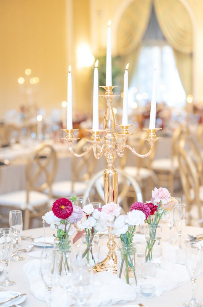 Gold candelabra centerpiece with lit taper candles surrounded by delicate pink and white blooms on a refined reception table at The Broadmoor in Colorado Springs.