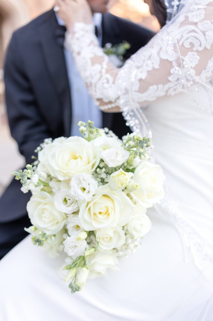 Intimate portrait of bride and groom embracing in a sunlit meadow, ivory rose bouquet in focus with lace gown details and soft mountain light in Colorado Springs.