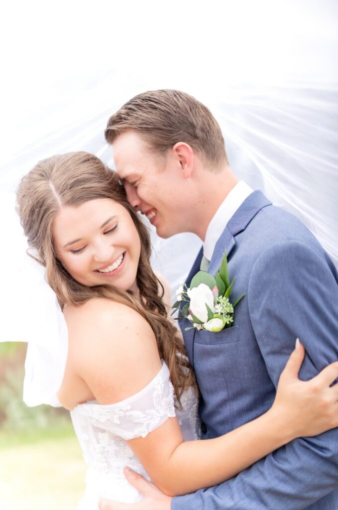 Romantic close-up of a bride and groom embracing on their Colorado wedding day, her veil softly flowing behind them as they share a joyful, intimate moment.